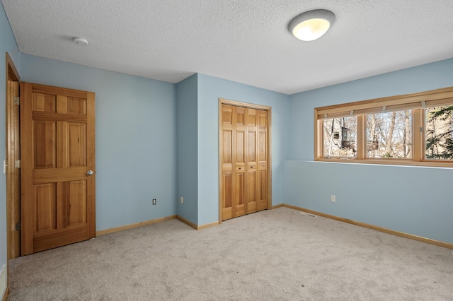 unfurnished bedroom featuring a closet, a textured ceiling, baseboards, and carpet