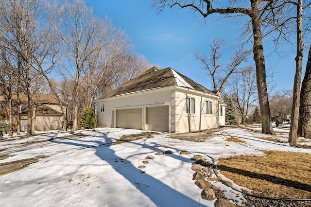 view of snowy exterior with stucco siding and an attached garage