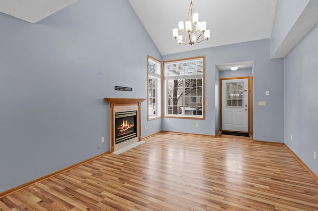 unfurnished living room featuring light wood-type flooring, a tiled fireplace, high vaulted ceiling, and an inviting chandelier