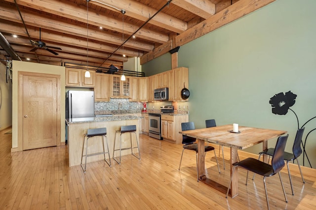 kitchen featuring light wood finished floors, stainless steel appliances, tasteful backsplash, glass insert cabinets, and a kitchen island