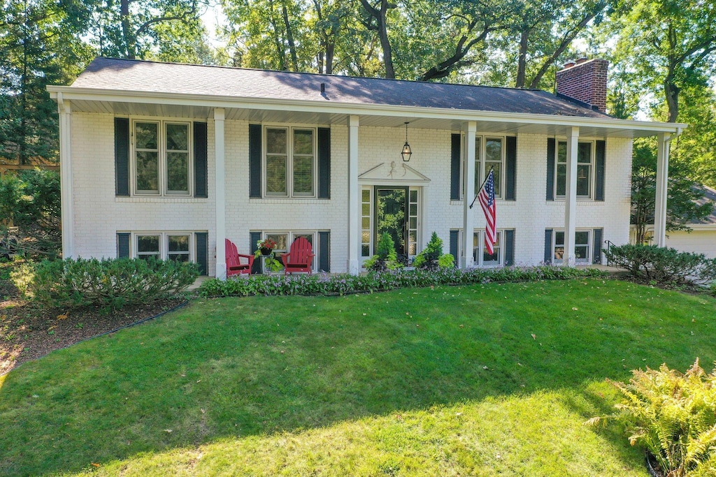 raised ranch with a porch, a chimney, a front lawn, and brick siding