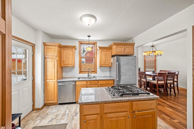 kitchen with sink, pendant lighting, a kitchen island, light hardwood / wood-style floors, and stainless steel appliances