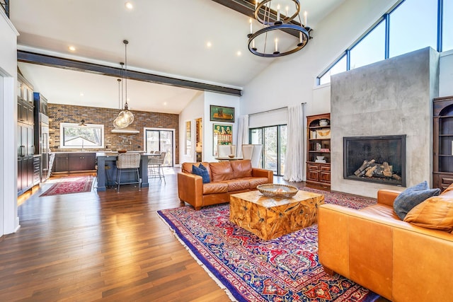 living room featuring high vaulted ceiling, dark wood-type flooring, a notable chandelier, brick wall, and a fireplace