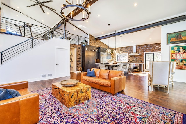 living room featuring visible vents, brick wall, wood finished floors, a notable chandelier, and high vaulted ceiling