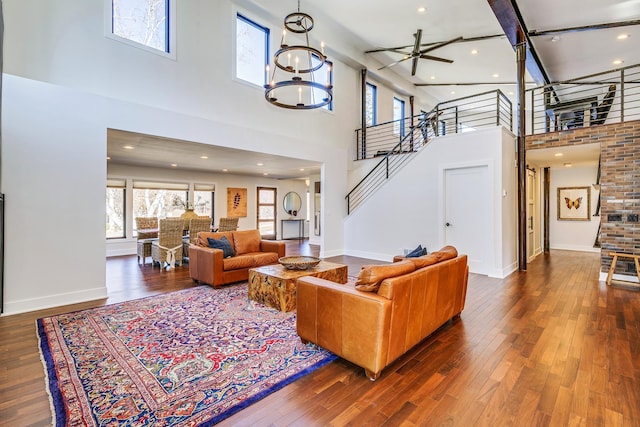 living room with ceiling fan with notable chandelier, hardwood / wood-style floors, a high ceiling, baseboards, and stairs