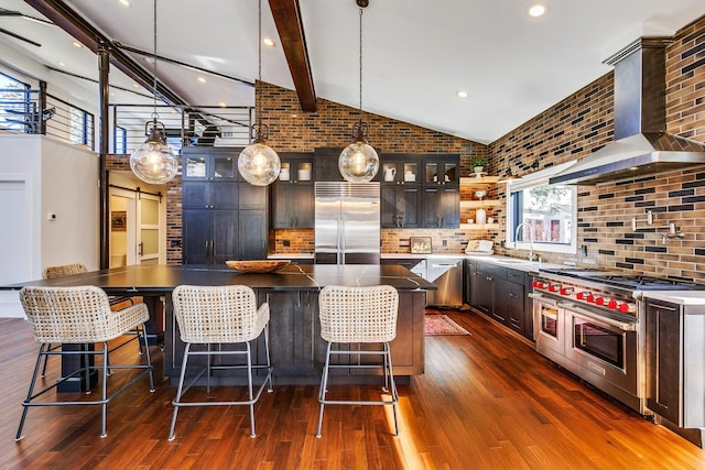 kitchen featuring a sink, premium appliances, dark wood finished floors, a barn door, and wall chimney exhaust hood