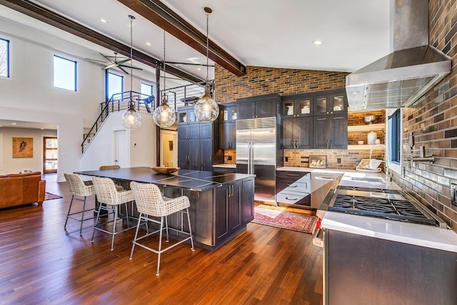 kitchen featuring beamed ceiling, a sink, dark wood finished floors, appliances with stainless steel finishes, and wall chimney exhaust hood