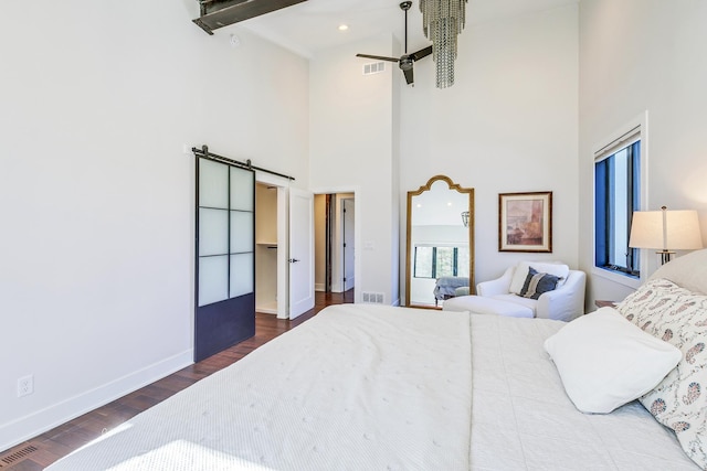 bedroom featuring wood finished floors, visible vents, baseboards, a high ceiling, and a barn door