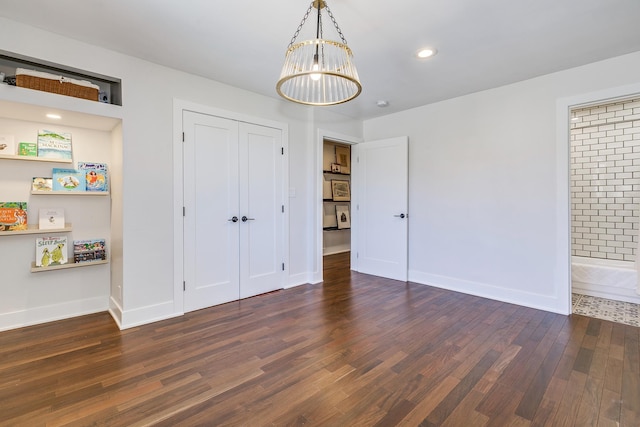 unfurnished bedroom with wood finished floors, recessed lighting, a closet, an inviting chandelier, and baseboards