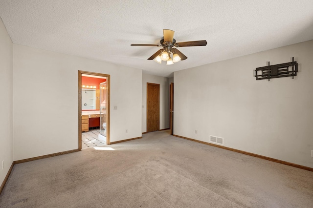 unfurnished bedroom with light colored carpet, visible vents, a textured ceiling, ensuite bath, and baseboards