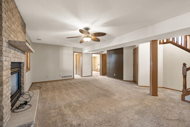 unfurnished living room featuring light carpet, visible vents, ceiling fan, a textured ceiling, and a stone fireplace