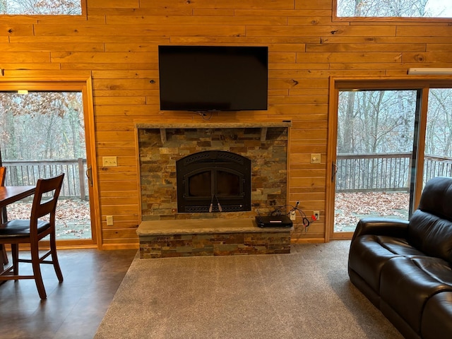 living room featuring dark carpet, wooden walls, and a stone fireplace