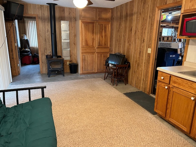 interior space with light carpet, a wood stove, wood walls, and ceiling fan