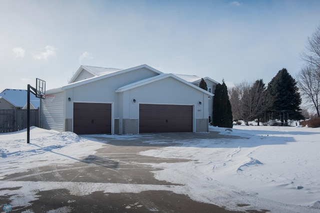 view of snowy exterior with an attached garage and fence