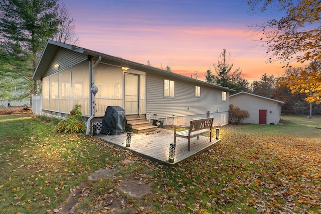 back house at dusk featuring a yard, a deck, a sunroom, and an outdoor structure