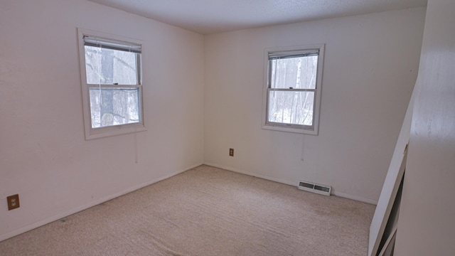 empty room featuring baseboards, a healthy amount of sunlight, visible vents, and light colored carpet