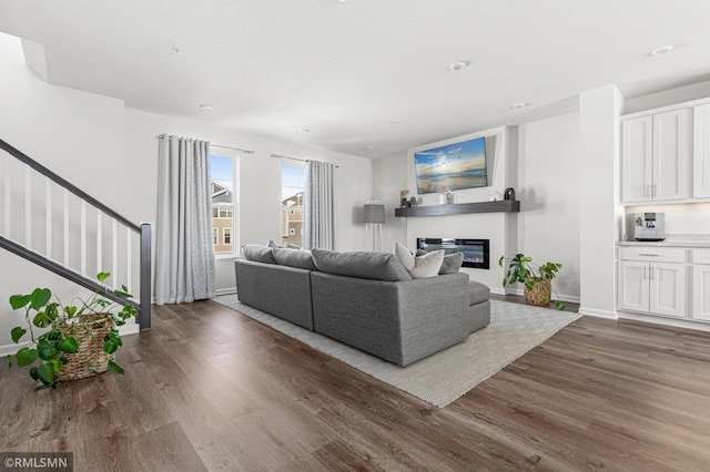 living area featuring dark wood-type flooring, stairway, a glass covered fireplace, and baseboards