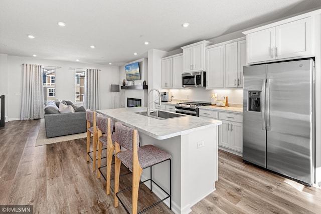 kitchen with an island with sink, stainless steel appliances, light countertops, white cabinetry, and a sink