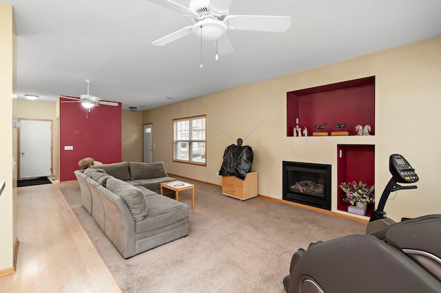 living room with ceiling fan, baseboards, a textured ceiling, and a glass covered fireplace