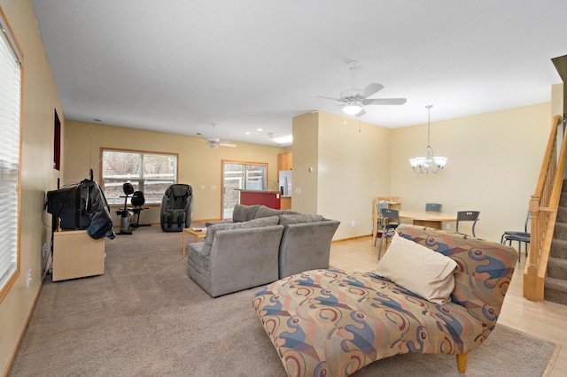 living room with light colored carpet, stairway, baseboards, and ceiling fan with notable chandelier