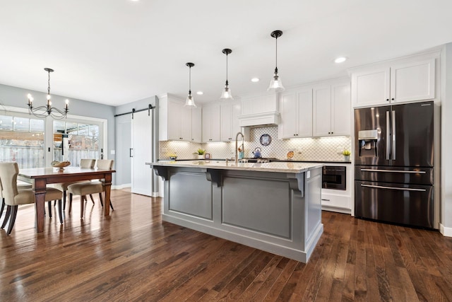 kitchen with dark wood-style floors, decorative backsplash, a barn door, white cabinetry, and stainless steel fridge