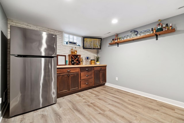 kitchen featuring brick wall, baseboards, freestanding refrigerator, open shelves, and light wood finished floors