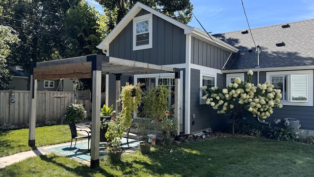 back of property with a patio, a shingled roof, fence, a yard, and board and batten siding