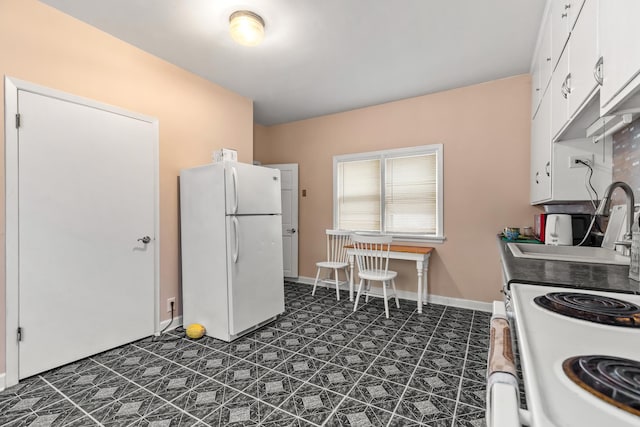 kitchen with dark floors, white cabinets, a sink, white appliances, and baseboards