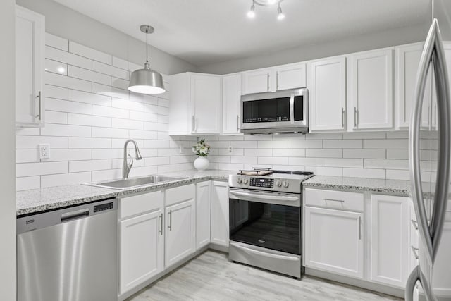 kitchen featuring decorative backsplash, appliances with stainless steel finishes, light wood-style floors, white cabinetry, and a sink