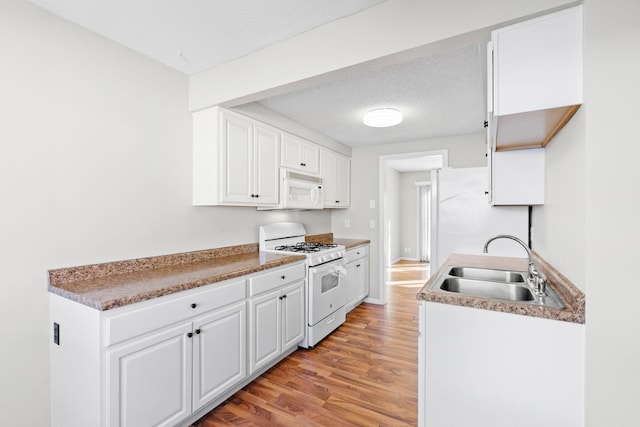 kitchen featuring white appliances, sink, white cabinetry, a textured ceiling, and light hardwood / wood-style floors