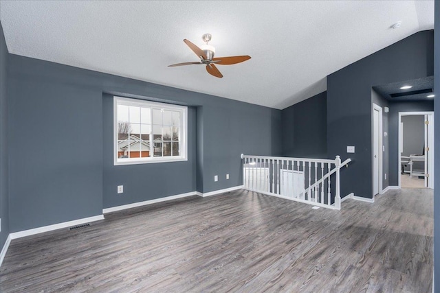 unfurnished room with lofted ceiling, a textured ceiling, wood finished floors, visible vents, and baseboards