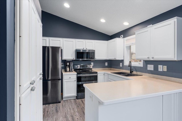 kitchen with appliances with stainless steel finishes, a peninsula, vaulted ceiling, light countertops, and a sink