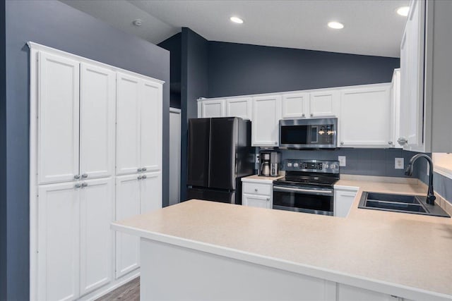 kitchen with lofted ceiling, a peninsula, stainless steel appliances, light countertops, and a sink