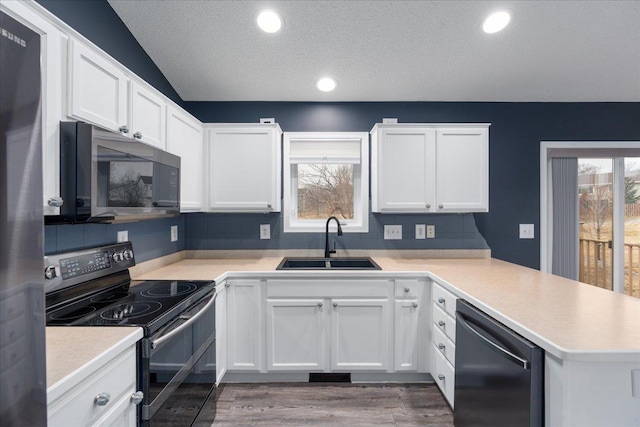 kitchen featuring light countertops, black electric range oven, a sink, dishwasher, and a peninsula