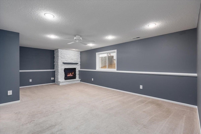 unfurnished living room with ceiling fan, a stone fireplace, visible vents, baseboards, and carpet