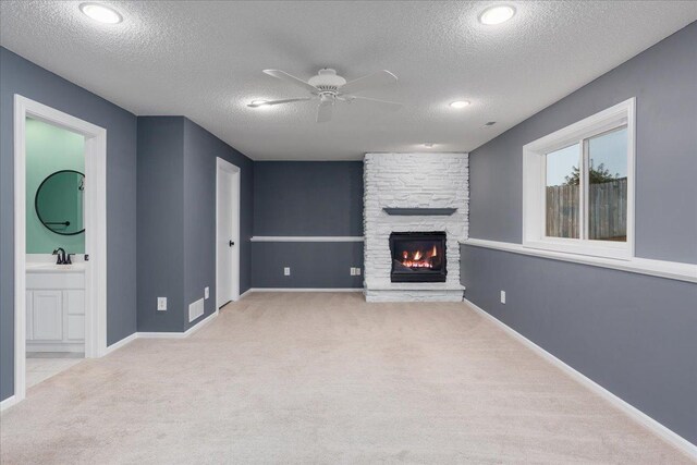 unfurnished living room featuring ceiling fan, a stone fireplace, a textured ceiling, and carpet flooring