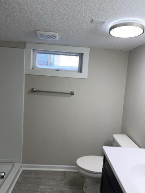 bathroom with a textured ceiling, toilet, vanity, and a shower