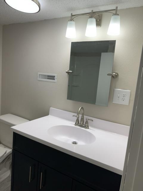 bathroom featuring a textured ceiling, toilet, and vanity