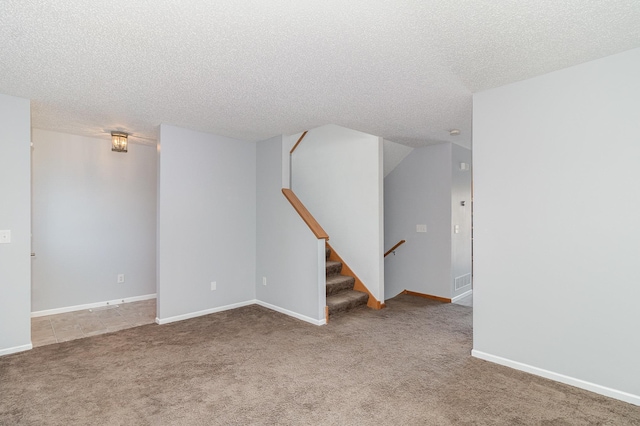 carpeted empty room featuring stairway, a textured ceiling, and baseboards