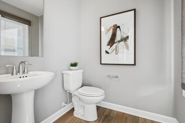 half bathroom with a sink, baseboards, toilet, and wood finished floors