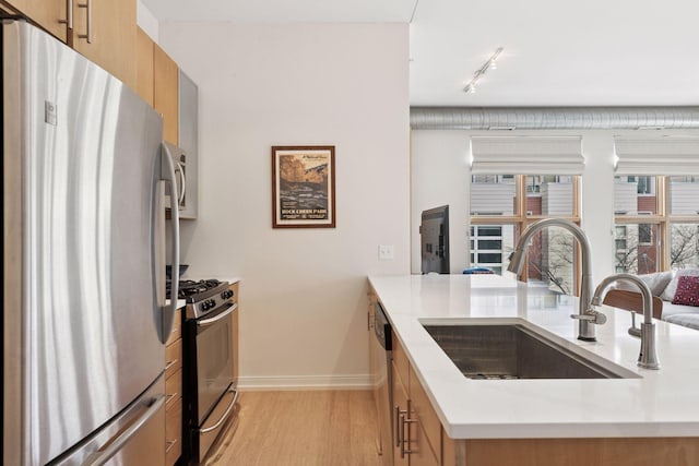 kitchen with stainless steel appliances, a sink, light countertops, light wood-type flooring, and modern cabinets