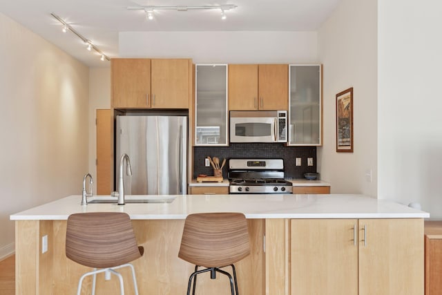 kitchen featuring a breakfast bar area, stainless steel appliances, a sink, light countertops, and tasteful backsplash