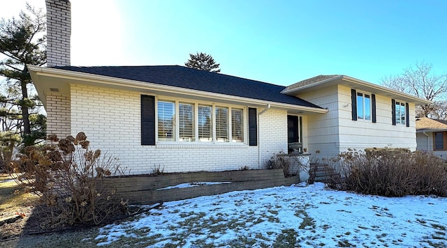 split level home featuring a chimney and brick siding