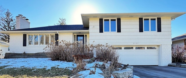 tri-level home featuring driveway, a garage, a chimney, and brick siding