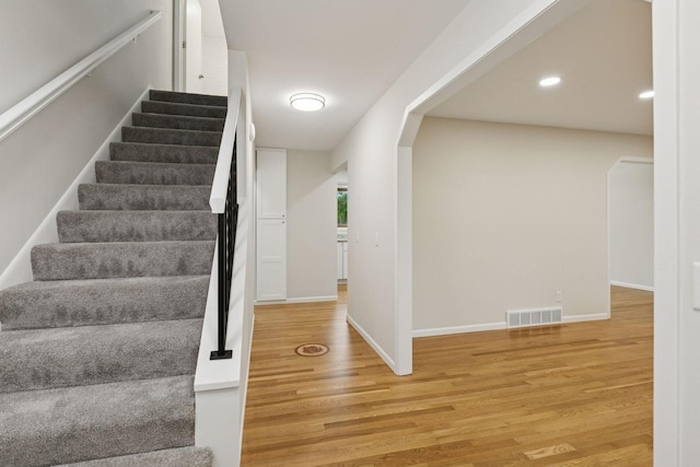 staircase with arched walkways, wood finished floors, baseboards, and recessed lighting