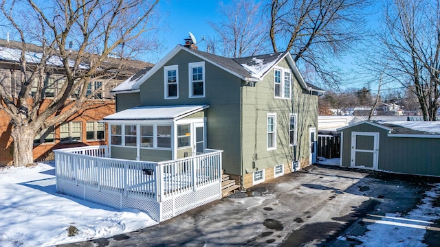 snow covered rear of property featuring a wooden deck, a chimney, a storage unit, and an outbuilding