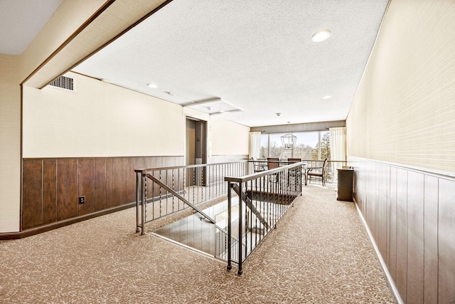 hall featuring wood walls, a textured ceiling, and light colored carpet