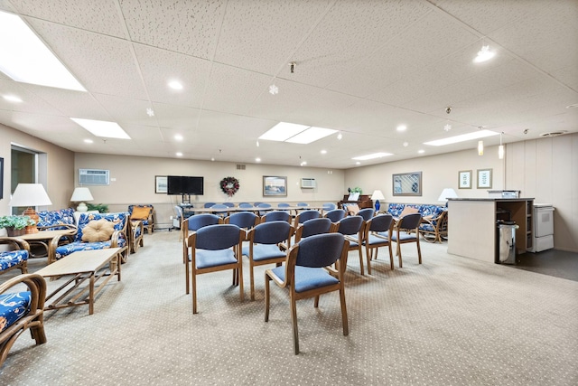 dining space with a paneled ceiling, light colored carpet, and a wall mounted air conditioner