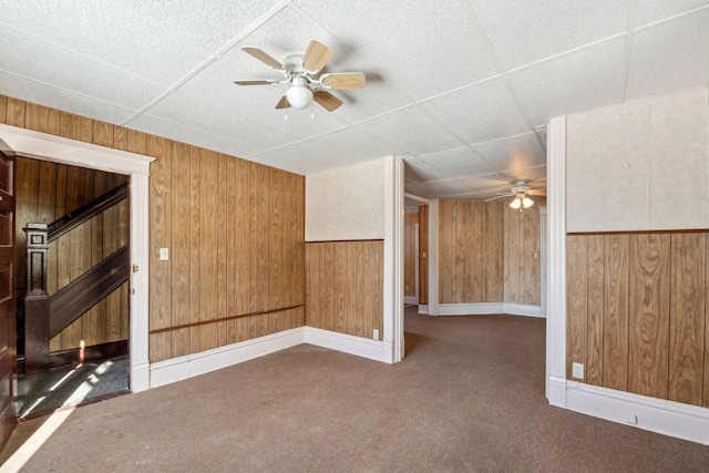 empty room featuring baseboards, ceiling fan, dark colored carpet, a paneled ceiling, and wood walls