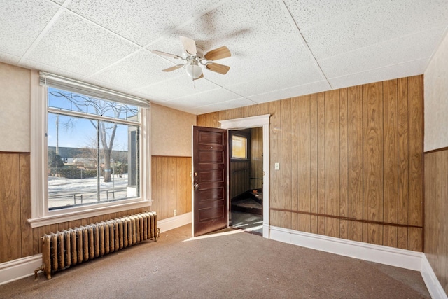 unfurnished room with ceiling fan, wooden walls, carpet, and radiator